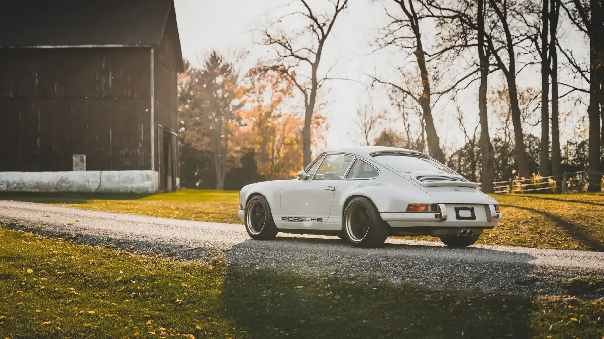 Restaurierter Porsche 911 Singer Novato-Commission in Dolphin Grey, seitlich fotografiert auf einer herbstlichen Landstraße vor einer Scheune.