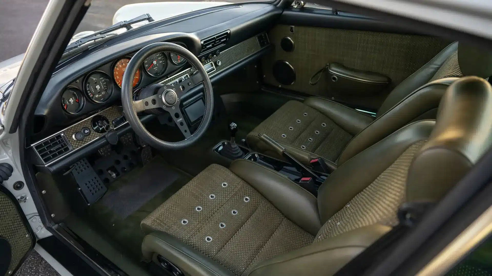 Innenraum eines restaurierten Porsche 911 (Type 964) von Singer mit Olivgrünem Leder und textilen Sitzflächen.