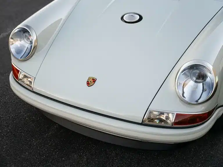 Detailaufnahme der Front eines in Dolphin Grey lackierten Porsche 911 von Singer auf Basis des Typs 964, mit Porsche-Wappen.