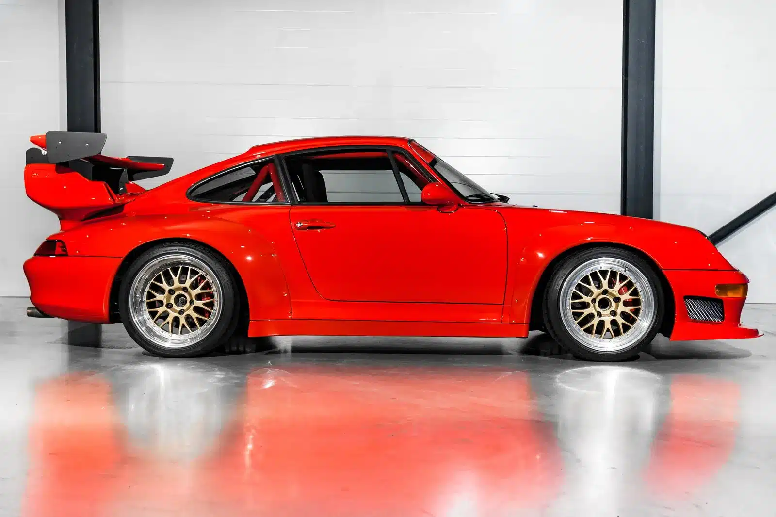 Porsche 993 Turbo GT2 Evo Umbau in Guards Red mit großem Heckflügel, goldenen BBS-Magnesium-Felgen und verbreiterter Karosserie in einer Halle.