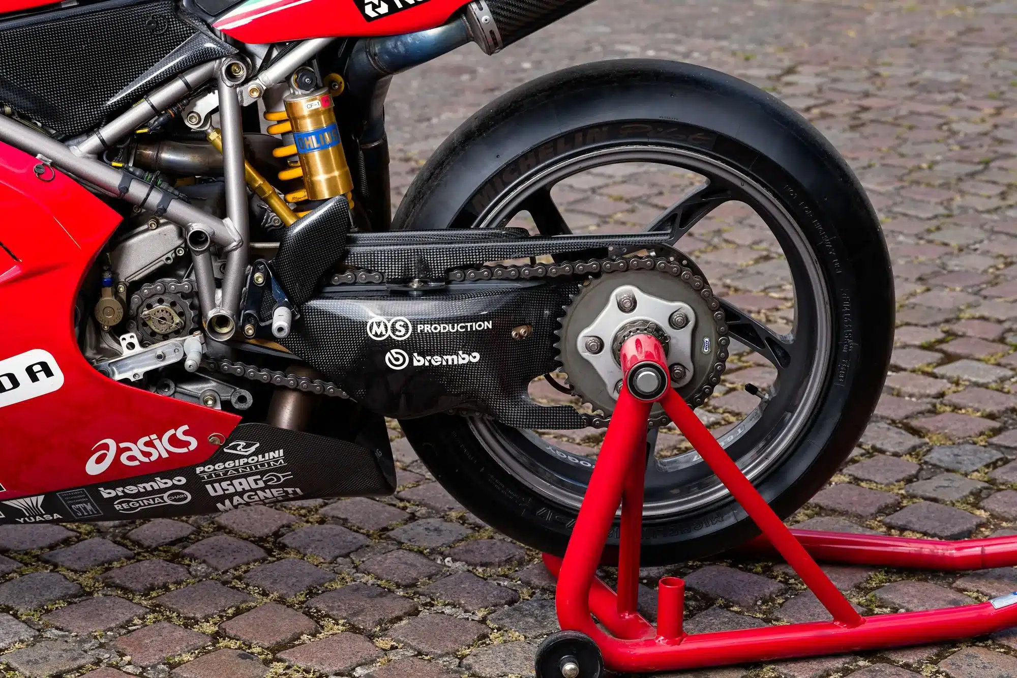 Nahaufnahme der hinteren Radaufhängung, Kettenantrieb und Schwinge einer Ducati 996 Superbike, ausgestellt auf Kopfsteinpflaster.
