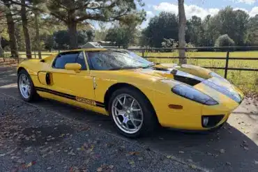 Gelber 2006 Ford GT mit schwarzen Streifen, geparkt im Freien vor Bäumen und einer Wiese