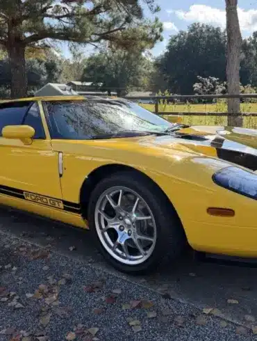 Gelber 2006 Ford GT mit schwarzen Streifen, geparkt im Freien vor Bäumen und einer Wiese