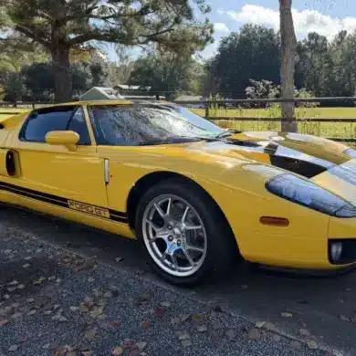 Gelber 2006 Ford GT mit schwarzen Streifen, geparkt im Freien vor Bäumen und einer Wiese