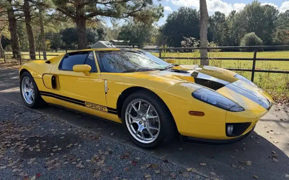Gelber 2006 Ford GT mit schwarzen Streifen, geparkt im Freien vor Bäumen und einer Wiese