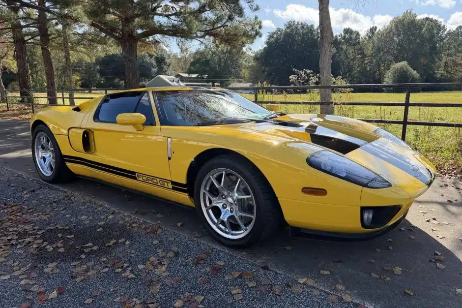 Gelber 2006 Ford GT mit schwarzen Streifen, geparkt im Freien vor Bäumen und einer Wiese