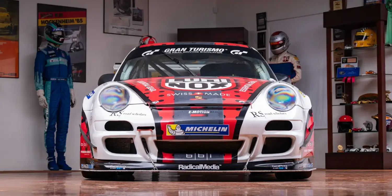 2007 Porsche 911 GT3 Cup Rennwagen, frontal aufgenommen, mit rotem und schwarzem Renn-Design und Sponsorlogos, in einer Motorsport-Garage.