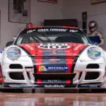 2007 Porsche 911 GT3 Cup Rennwagen, frontal aufgenommen, mit rotem und schwarzem Renn-Design und Sponsorlogos, in einer Motorsport-Garage.