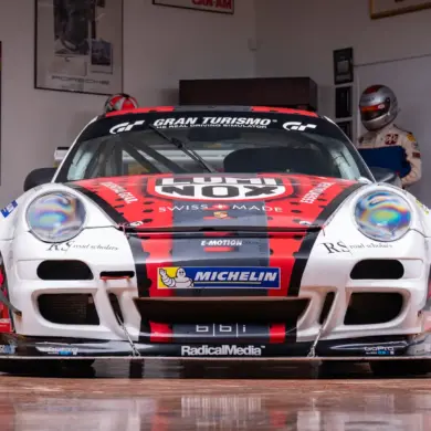 2007 Porsche 911 GT3 Cup Rennwagen, frontal aufgenommen, mit rotem und schwarzem Renn-Design und Sponsorlogos, in einer Motorsport-Garage.