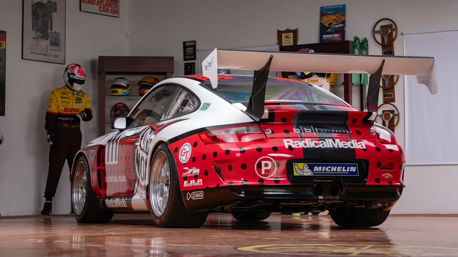 2007 Porsche 911 GT3 Cup mit Rennlackierung und Heckflügel in einer Garage, umgeben von Helmen und Rennmemorabilia.