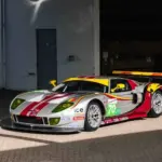 Silberner Ford GT1 by Matech Rennwagen von 2010 mit roten und gelben Akzenten vor einer Garage.