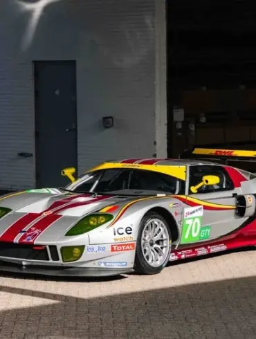 Silberner Ford GT1 by Matech Rennwagen von 2010 mit roten und gelben Akzenten vor einer Garage.