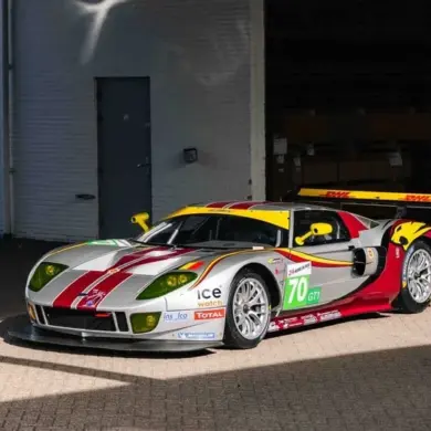 Silberner Ford GT1 by Matech Rennwagen von 2010 mit roten und gelben Akzenten vor einer Garage.