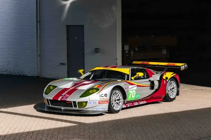Silberner Ford GT1 by Matech Rennwagen von 2010 mit roten und gelben Akzenten vor einer Garage.