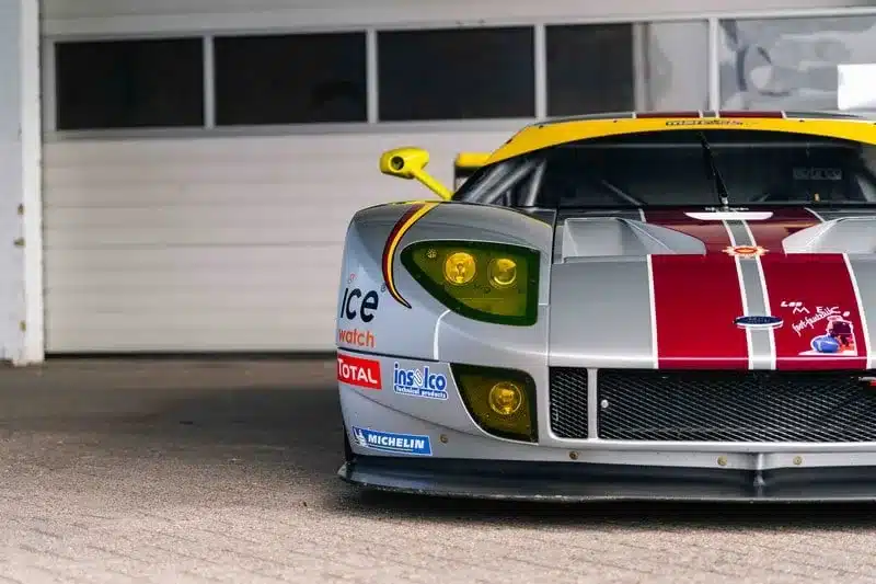Frontansicht eines silber-roten Ford GT1-by-Matech aus dem Baujahr 2010 mit Rennbeklebung und gelben Scheinwerfern.