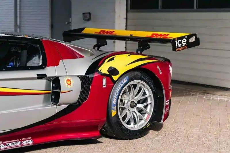 Heckpartie eines silber-roten Ford GT1-by-Matech mit markantem Heckflügel und Motorsport-Bereifung vor einer Garage.