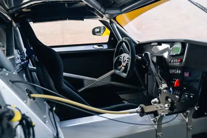 Cockpitansicht eines silbernen GT1-by-Matech-Rennwagens aus dem Jahr 2010, detailreich mit Überrollkäfig, Rennsitz und Karbon-Armaturenbrett