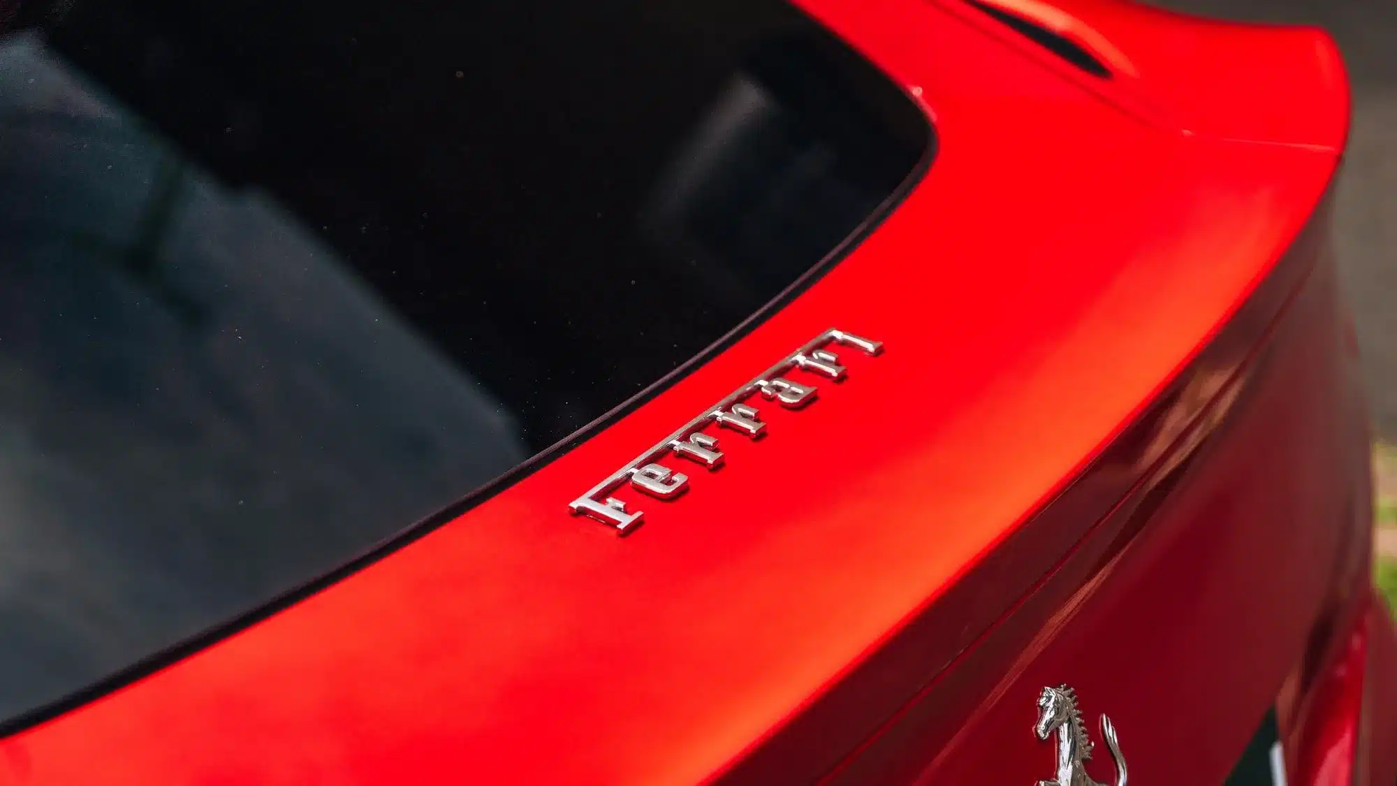 Rotes Heck eines Ferrari F12 mit dem Ferrarischriftzug und Pferdeemblem aus nächster Nähe.