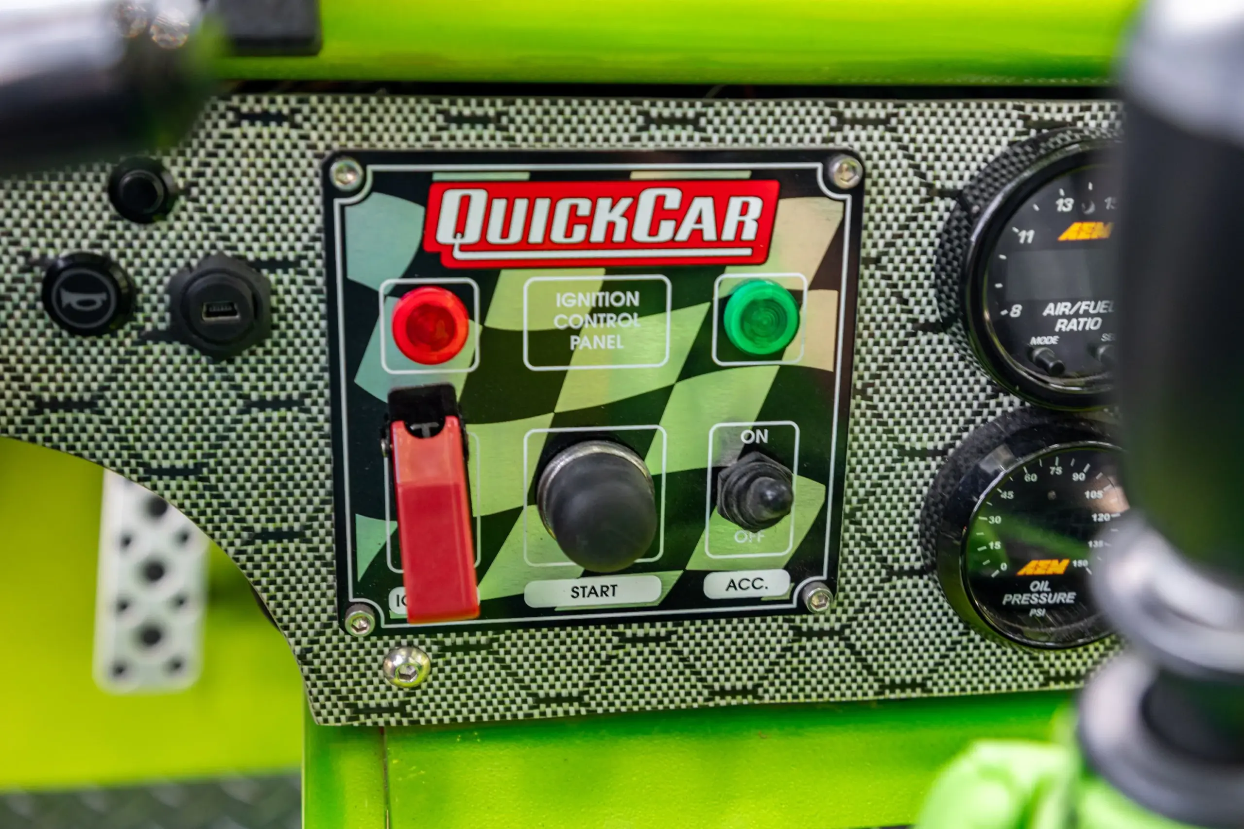 QuickCar-Zündpanel mit Schaltern und Kontrollleuchten im Cockpit des Exotruck GR, umgeben von Carbon-Look-Oberfläche.