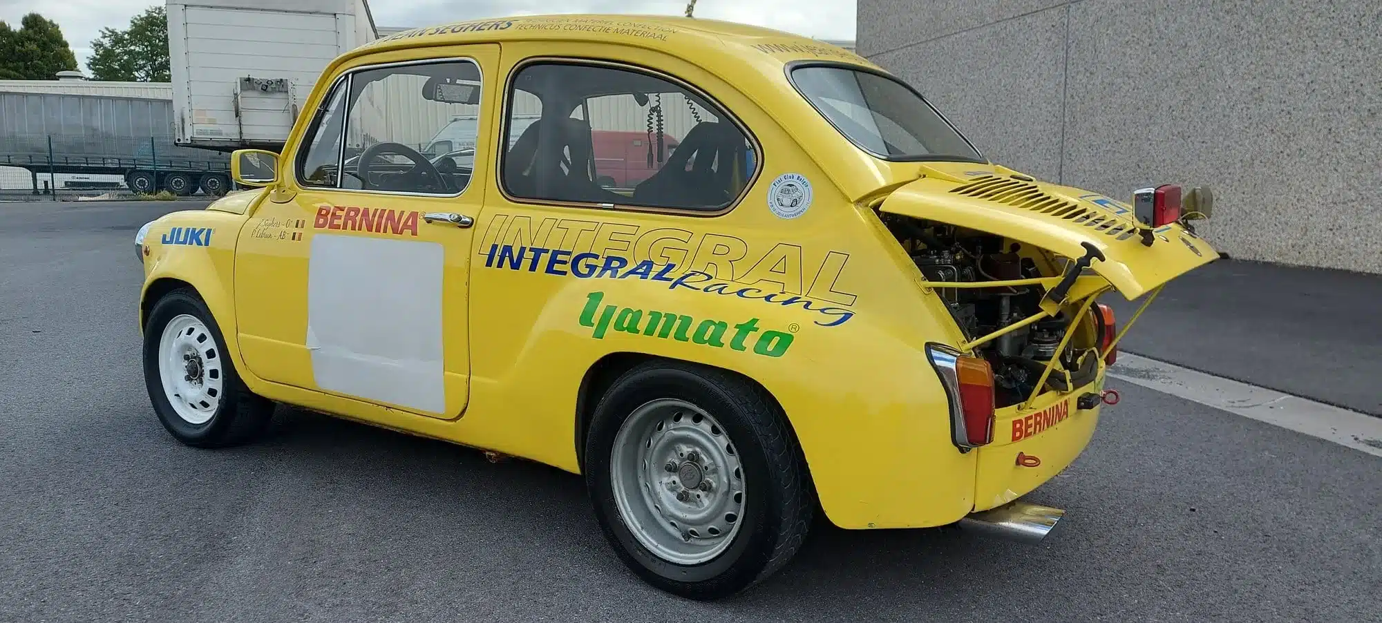 Seitenansicht eines gelben Abarth 600 1050 cm³ TC Replica mit Rennaufklebern und offenem Motorraum.