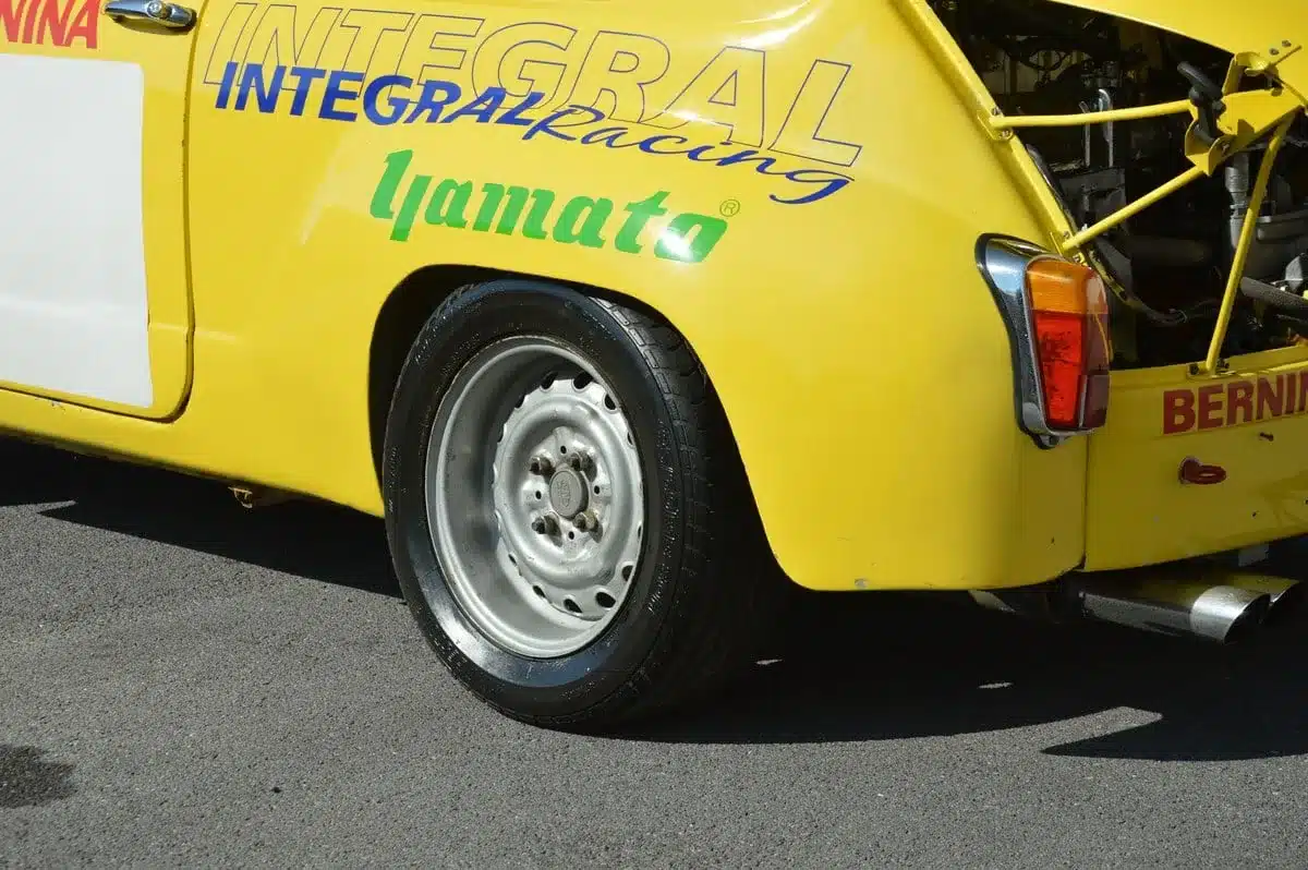 Gelber hinterer Radlauf mit Rennlackierung und Stahlfelge der Abarth 600 1050 cm³ TC Replica, Auspuff sichtbar.