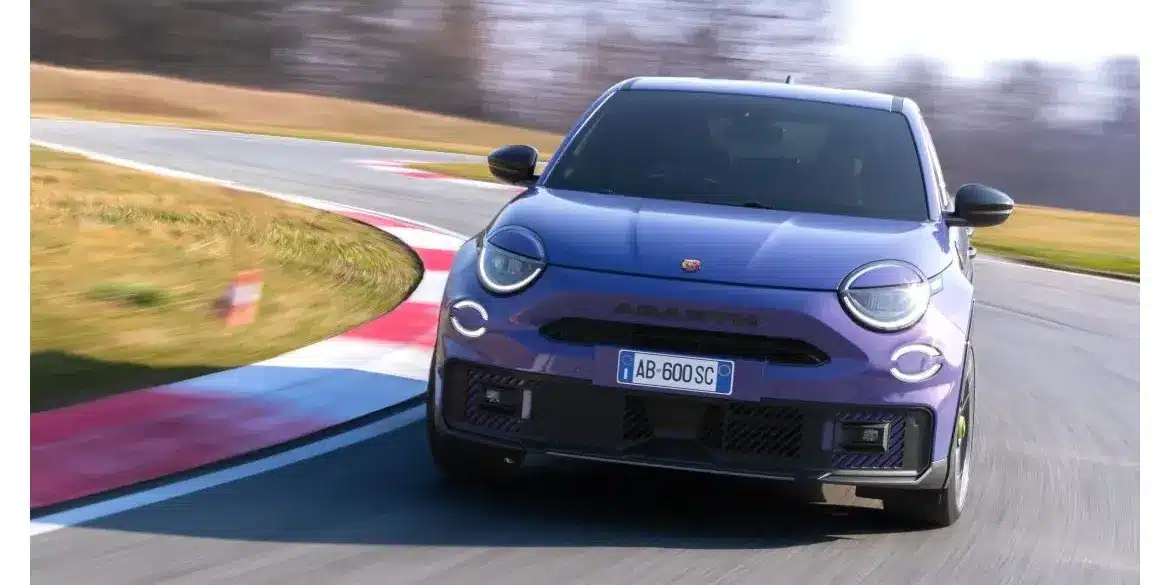 Frontansicht eines violetten Abarth 600e Scorpionissima auf einer Rennstrecke in Kurvenfahrt.