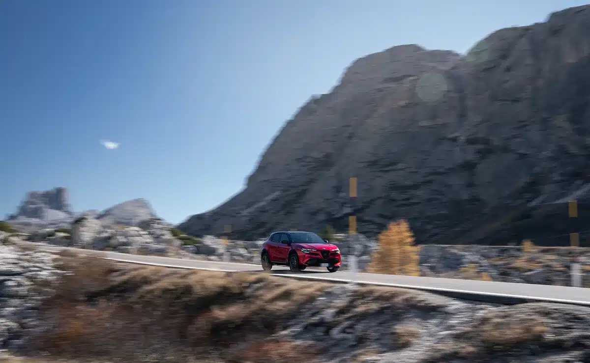 Der Alfa Romeo Junior Sport Speciale in Rot unterwegs auf einer Bergstraße, im Hintergrund felsige Berge und blauer Himmel.