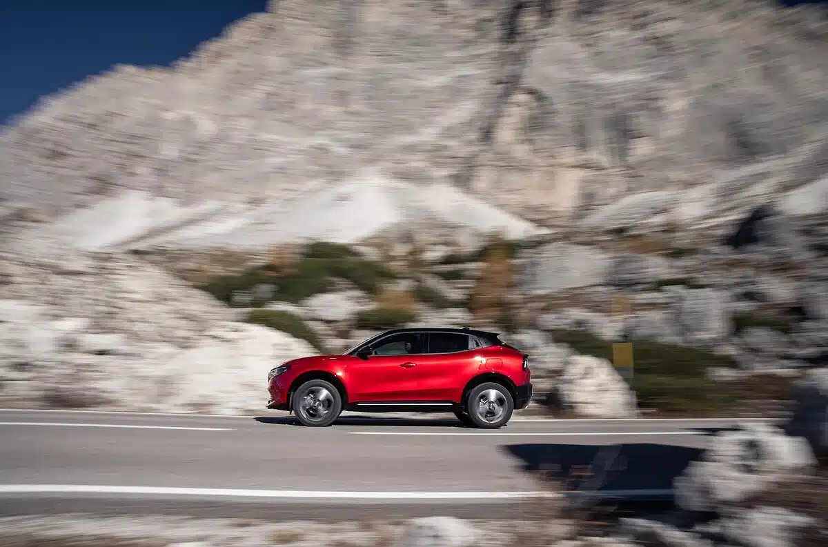 Roter Alfa Romeo Junior Sport Speciale fährt auf einer Straße vor felsiger Bergkulisse.