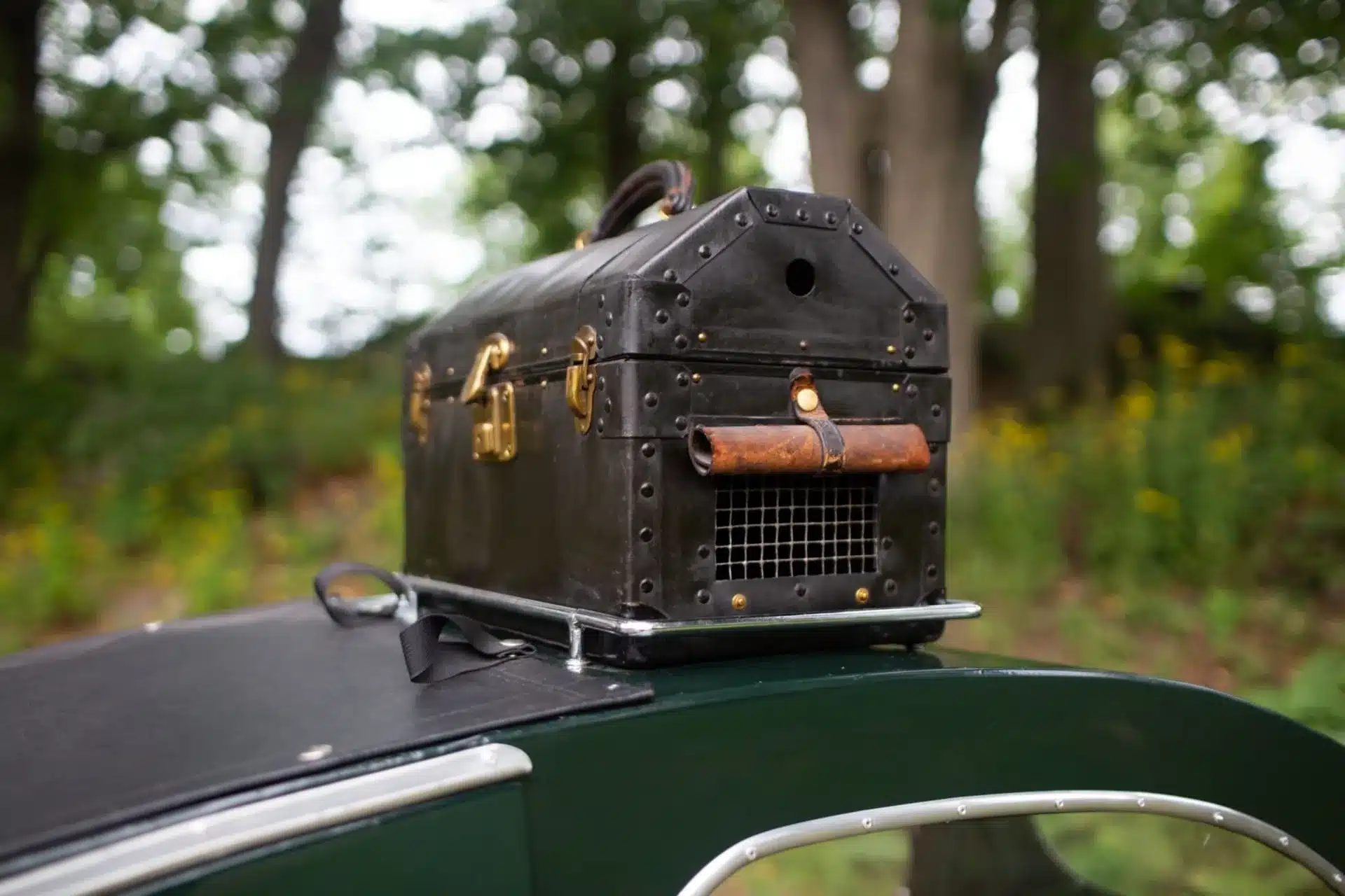 Schwarzer, antiker Lederkoffer mit Belüftungsgitter und Messingbeschlägen auf einem Fahrzeug-Seitenwagen.