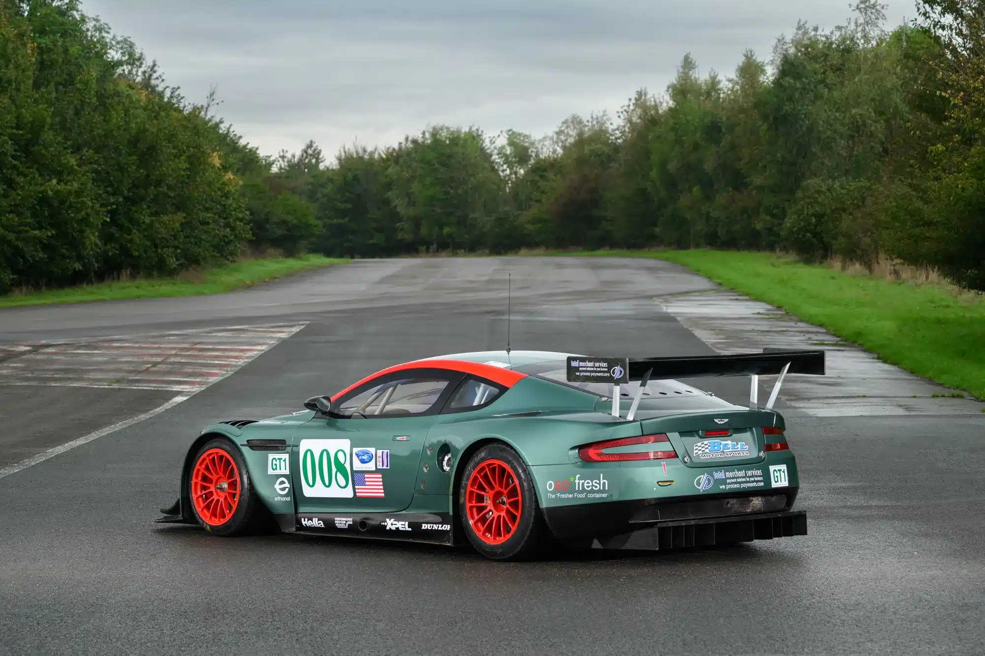 Aston Martin DBR9/5 GT1-Rennwagen aus dem Jahr 2006 mit Startnummer 008 und US-Flagge, von hinten aufgenommen auf nasser Asphaltstrecke.