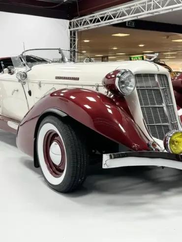 Auburn Speedster 6,7 V8 Cabriolet von 1979 in Weiß mit bordeauxfarbenen Kotflügeln und Chromdetails in einer Halle.