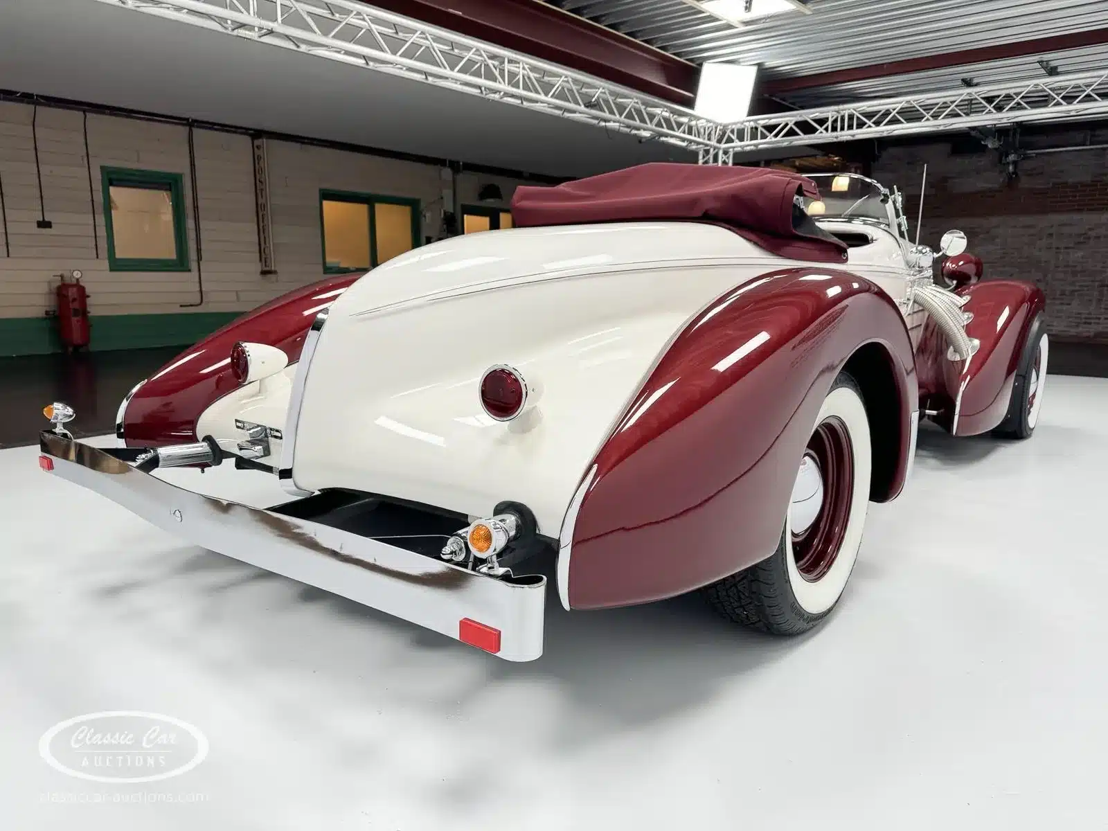 Heckansicht eines restaurierten Auburn Speedster 6,7 V8 Cabriolets von 1979 in Weiß mit bordeauxroten Kotflügeln und Verdeck, aufgenommen in einem Ausstellungsraum.