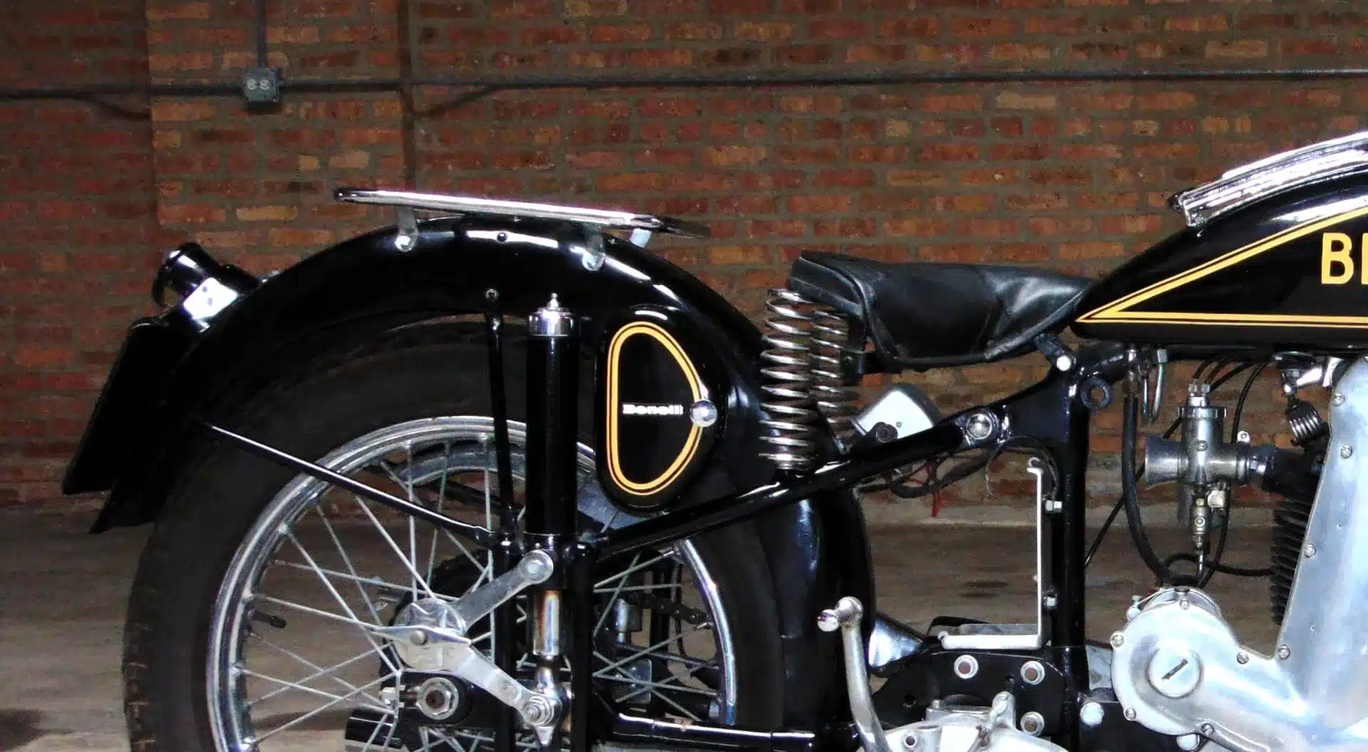 Seitliche Detailansicht des Hecks und Rahmens eines klassischen Benelli Einzylindermotorrads vor Backsteinwand.