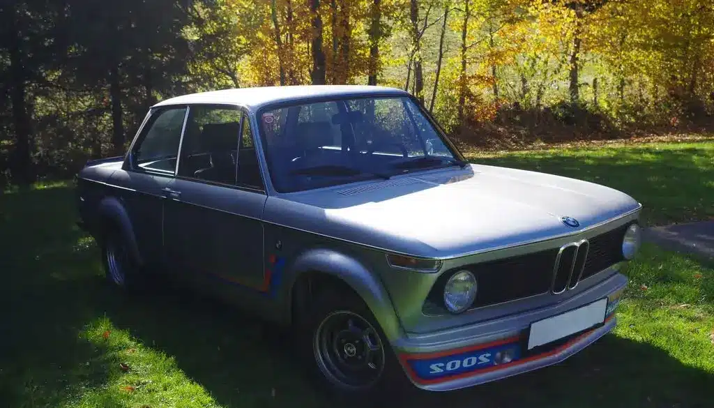 BMW 2002 Turbo von 1975 in silberner Lackierung, Seitenansicht mit markantem Frontspoiler auf einer grünen Wiese
