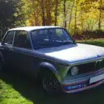 BMW 2002 Turbo von 1975 in silberner Lackierung, Seitenansicht mit markantem Frontspoiler auf einer grünen Wiese