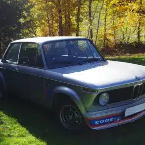 BMW 2002 Turbo von 1975 in silberner Lackierung, Seitenansicht mit markantem Frontspoiler auf einer grünen Wiese