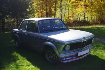 BMW 2002 Turbo von 1975 in silberner Lackierung, Seitenansicht mit markantem Frontspoiler auf einer grünen Wiese