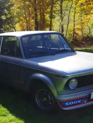 BMW 2002 Turbo von 1975 in silberner Lackierung, Seitenansicht mit markantem Frontspoiler auf einer grünen Wiese