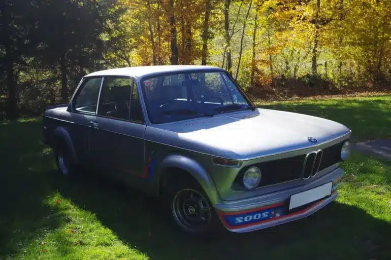 BMW 2002 Turbo von 1975 in silberner Lackierung, Seitenansicht mit markantem Frontspoiler auf einer grünen Wiese