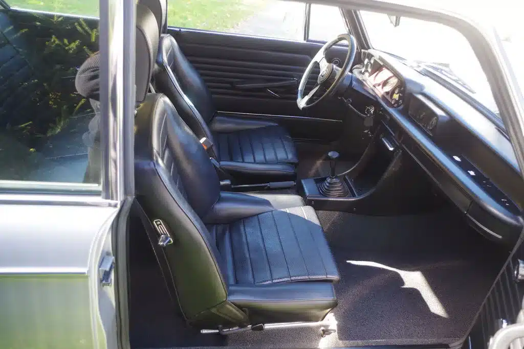 Innenansicht eines BMW 2002 Turbo von 1975 mit schwarzen Sitzen und klassischem Armaturenbrett.