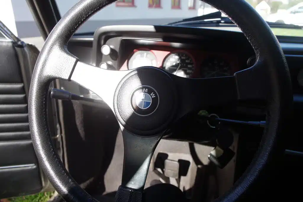 Blick auf das Lenkrad mit BMW-Logo und das Armaturenbrett eines BMW 2002 Turbo, Baujahr 1975.