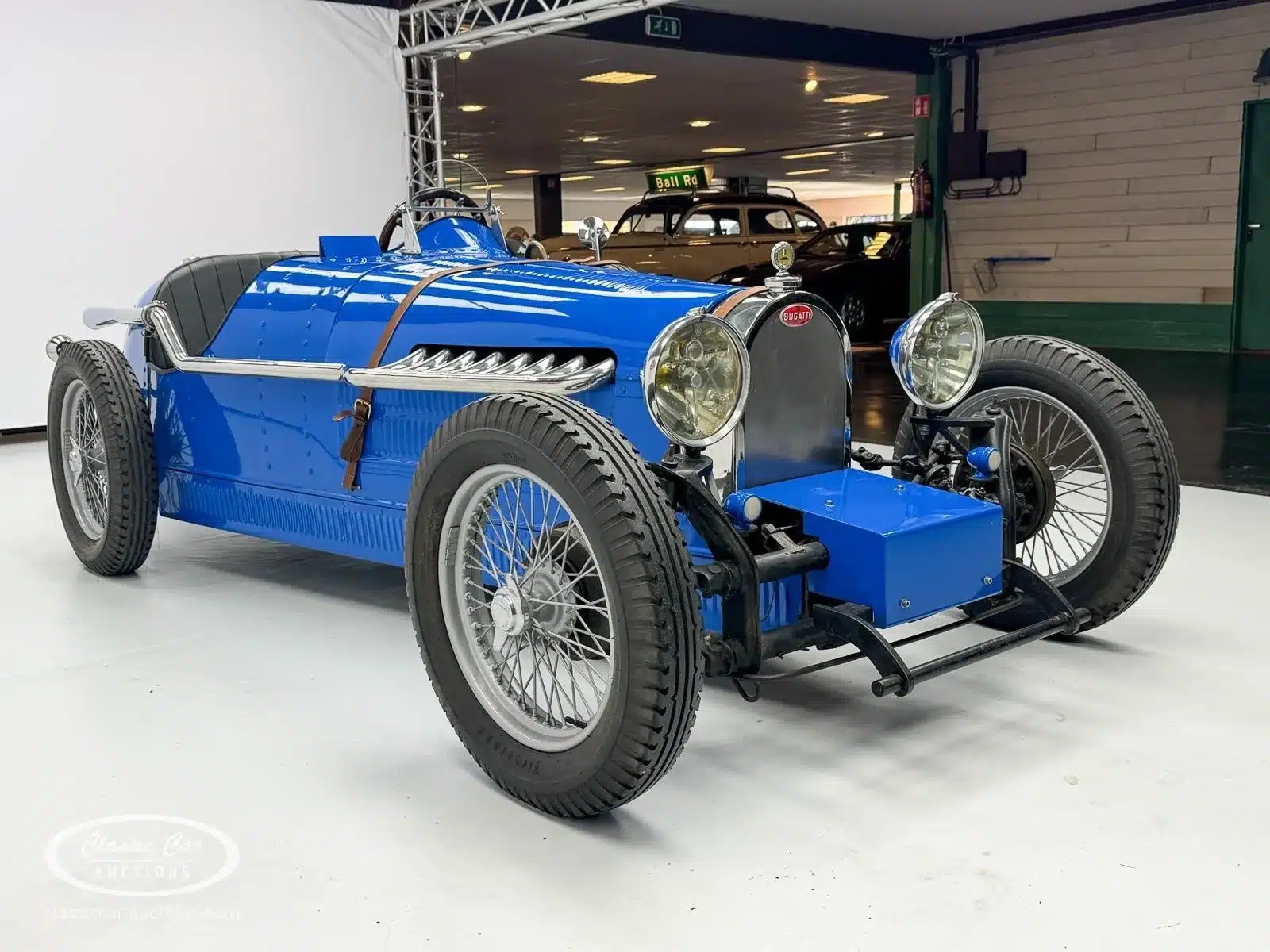 Seitenansicht eines blauen Bugatti Creation Cabriolets von 1971 mit schwarzen Ledersitzen, Speichenrädern und markantem Chromkühlergrill in einer Ausstellungshalle