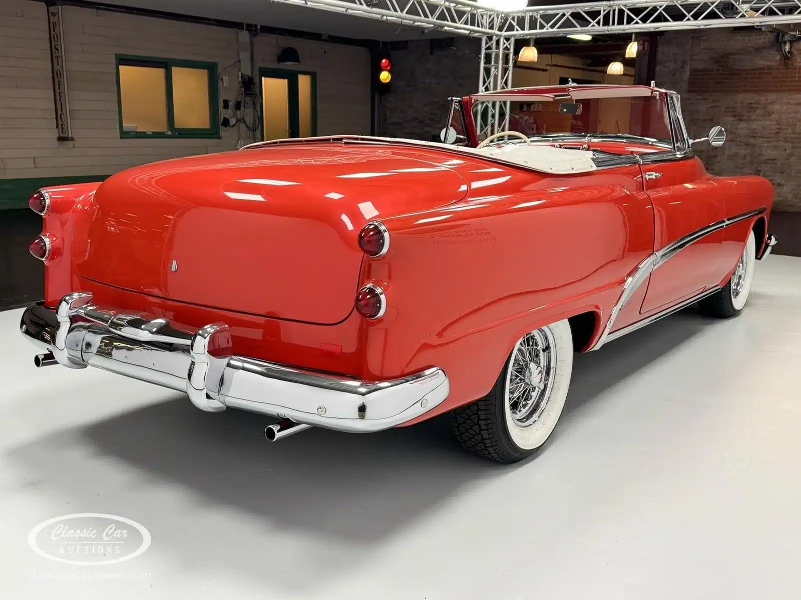 Heckansicht eines roten Buick Special 40 Cabriolets von 1953 auf einer Ausstellungsfläche mit weißem Interieur und klassischen Weißwandreifen.