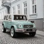 Frontansicht des Carlex G63 Lago Vintage in mintgrüner Lackierung auf Kopfsteinpflaster, parkend vor einem Altbau.