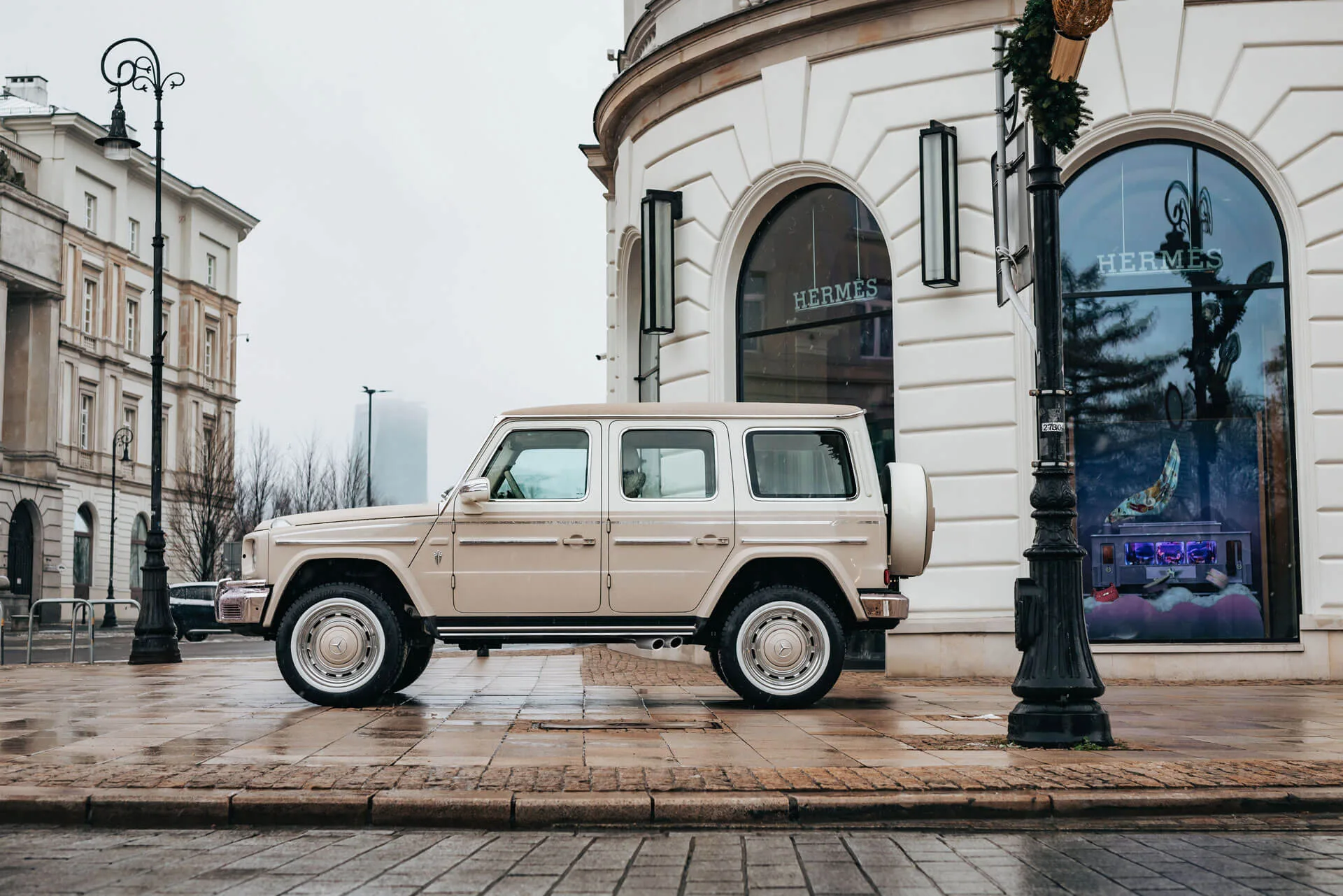 Sandfarbener Carlex G63 Sabbia Vintage Mercedes-Benz G-Klasse parkt vor einem eleganten Gebäude.