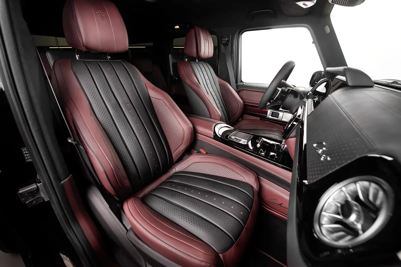 Nahaufnahme der Vordersitze und des Armaturenbretts im Carlex Rubino Vintage Interieur eines Mercedes-AMG G 63, mit handgefertigten Lederoberflächen in Bordeauxrot und Schwarz.