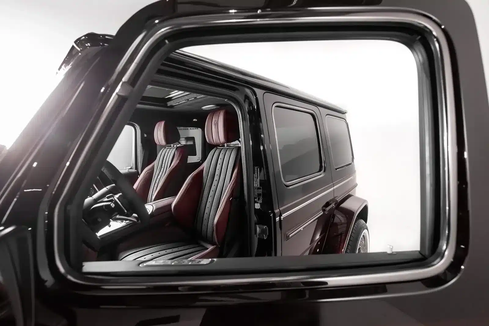 Blick durch das Seitenfenster auf das luxuriöse Interieur des Mercedes-AMG G 63 Carlex Rubino Vintage mit roten und schwarzen Ledersitzen.