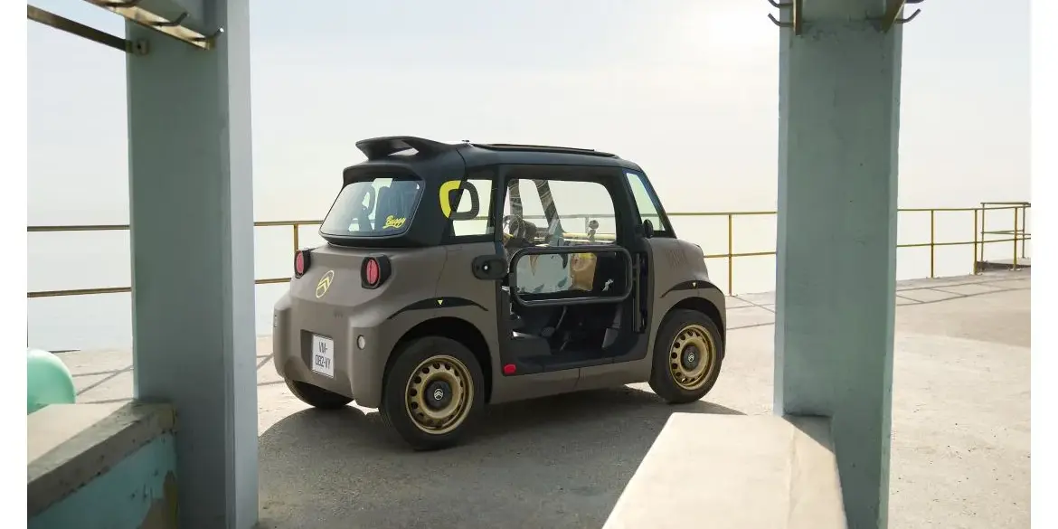 Citroën Ami Buggy Outdoor-Freizeitvariante mit offenem Dach und goldenen Felgen seitlich am Meer.