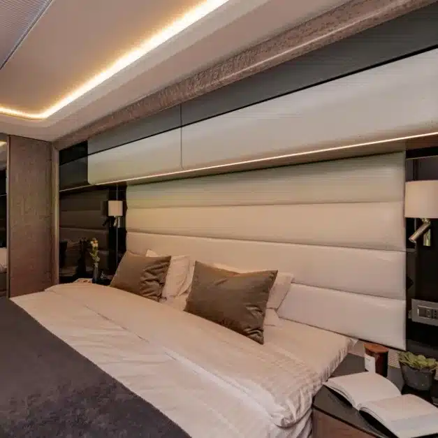 Schlafzimmer mit großem Bett, eleganter Holz- und Polsterwand sowie Premium-Beleuchtung in einem Luxus-Reisemobil.