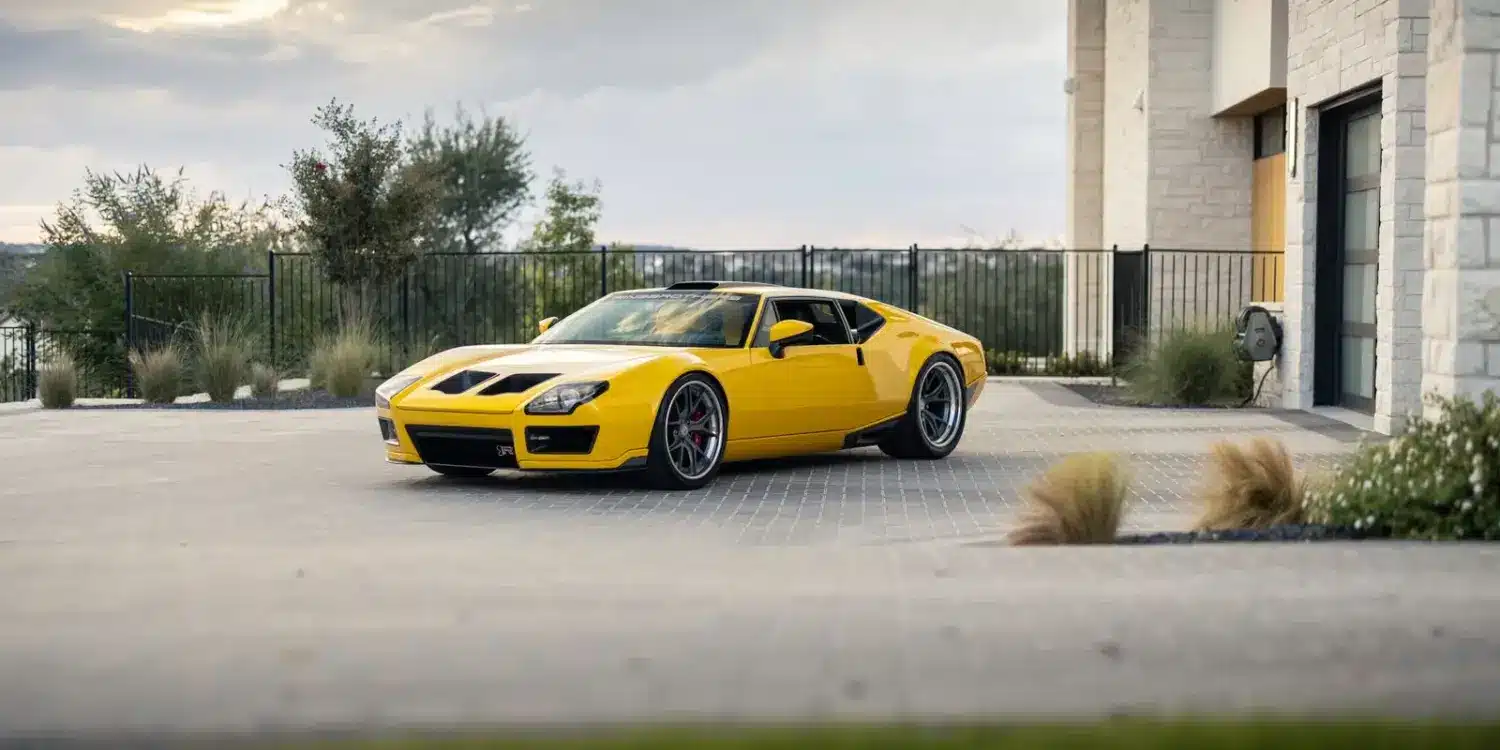 DeTomaso Pantera ADRNLN in Gelb, restauriert und getunt, steht vor einem modernen Haus bei Sonnenuntergang.